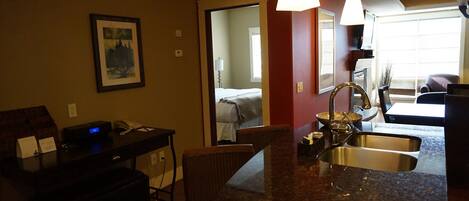 A hotel room with a kitchenette, a dining area, and a bed.