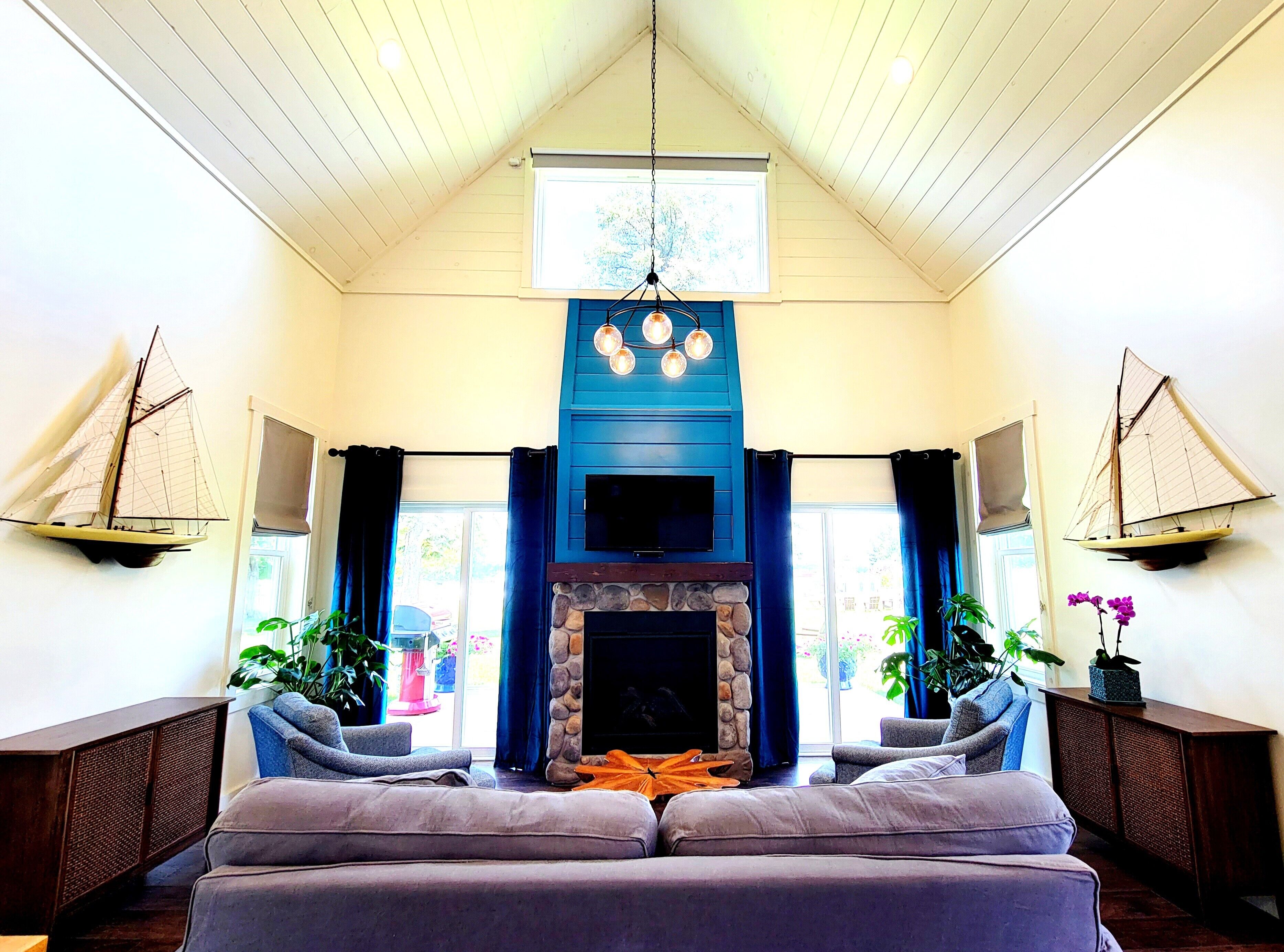 A cozy living room with a stone fireplace, a large window, and two sailboat wall decorations.