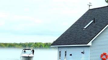 A house with a dock extending into calm water, a boat on the water, and a life preserver on the dock.