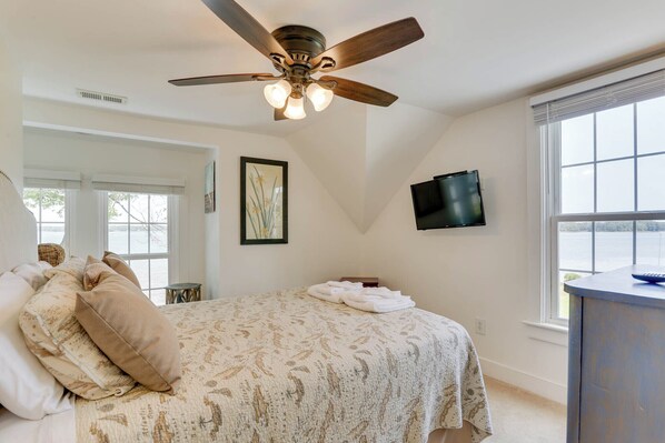 A bedroom with a bed, a ceiling fan, a TV, and a window with a view of the water. - Experience the Best of Mathews Riverfront Living here at Mariner's Legacy! (Bohannon)