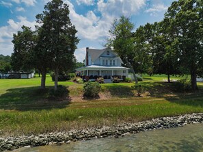 A large house with a porch, surrounded by trees and a grassy field. - Experience the Best of Mathews Riverfront Living here at Mariner's Legacy! (Bohannon)