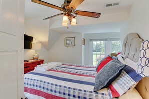 A bedroom with a bed, a ceiling fan, a TV, a bedside table, and a window with a view. - Experience the Best of Mathews Riverfront Living here at Mariner's Legacy! (Bohannon)