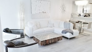 A modern living room with a white sofa, a coffee table, and a dining area with a chandelier. - POSHPADZ-Playa Blanca -Prime Jupiter Beach Location (Jupiter)