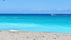 Une plage aux eaux turquoise et limpides, un navire au loin et un petit bateau.