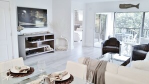 Un salon moderne doté d’un téléviseur à écran plat, d’un coin repas avec une table en verre et d’un balcon aménagé avec du mobilier d’extérieur.