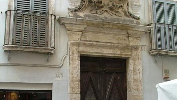 A building with a large wooden double door, a balcony with metal railings, and a decorative stone relief above the door. - PF Apartment 2 Bedroom- and you're in Piazza Navona CIN:IT058091C2SLMC5MBC (Roma)
