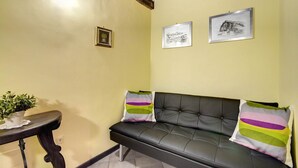 A cozy room with a dark leather sofa, two colorful pillows, a small table with a plant, and two framed pictures on the wall. - PF Apartment 2 Bedroom- and you're in Piazza Navona CIN:IT058091C2SLMC5MBC (Roma)