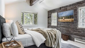 A bedroom with a bed, pillows, a blanket, a picture on the wall, and a window.