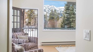 A cozy room with a gray sofa, a white rug, and a large window offering a mountain view.