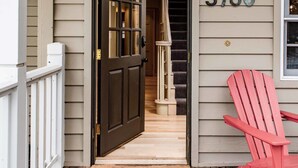A wooden porch with a red Adirondack chair, a door leading to a staircase, and a mailbox with the number 3780.