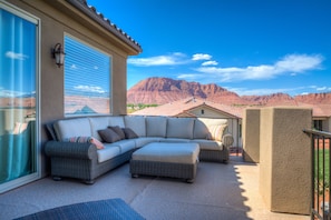 A covered outdoor seating area with a sectional sofa and ottoman, a sliding glass door, and a view of red rock formations.