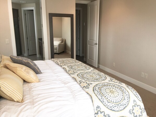A bedroom with a large bed, a chair, and a door leading to another room.