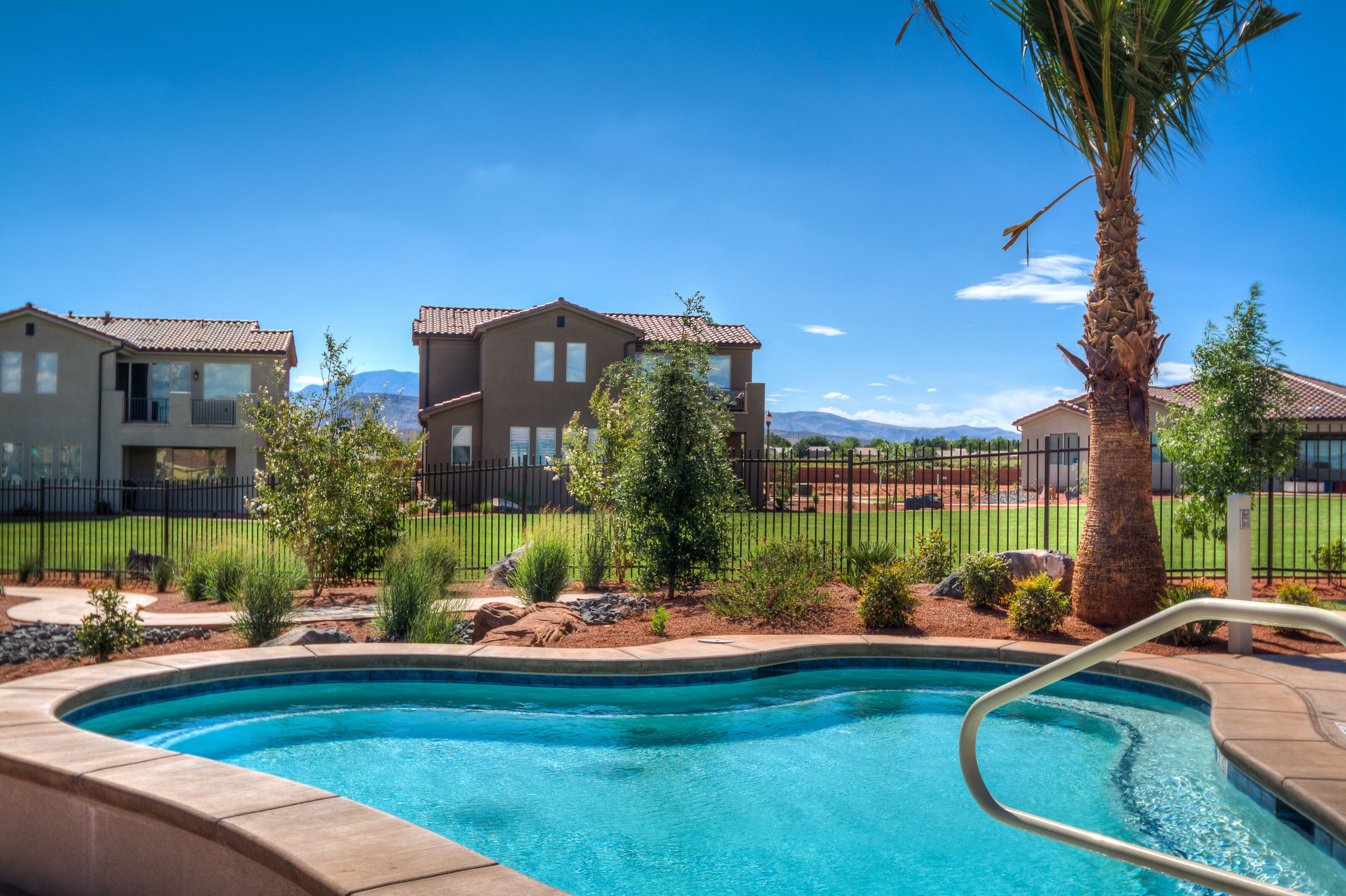 A swimming pool with a palm tree and a fence, surrounded by a landscaped garden and residential buildings.