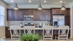Une cuisine moderne avec des meubles en bois foncé, des appareils électroménagers en acier inoxydable et des luminaires suspendus.