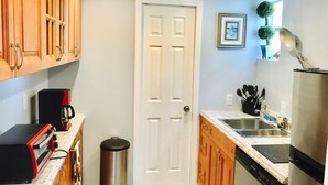 Una cocina compacta con armarios de madera, un refrigerador de acero inoxidable, una cafetera y un lavamanos.