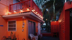 Un edificio con fachada roja, un balcón con luces colgantes y una pequeña zona de estar al aire libre con sillas de mimbre.
