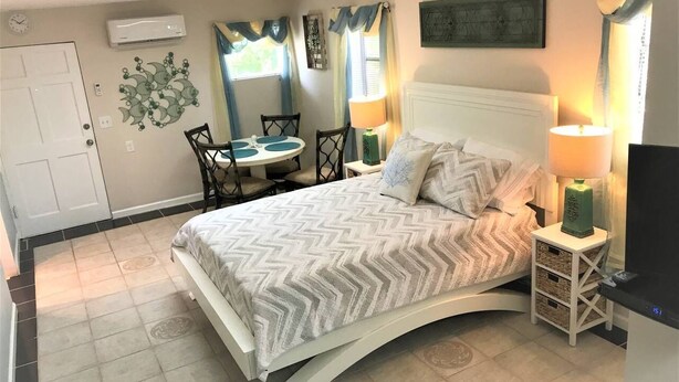 Un dormitorio con cama, mesitas de noche, una silla, escritorio y ventana con cortinas.