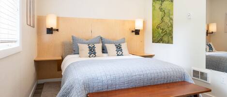 A neatly arranged bedroom with a bed, bedside tables, a bench, and artwork on the wall.