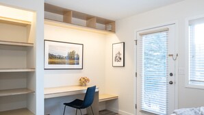 Un dormitorio con cama, escritorio y silla, y una puerta con persianas.