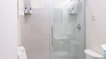 Ein modernes Badezimmer mit einer gläsernen Duschkabine, einer Toilette und einem Waschtisch mit Spiegel.