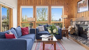 A cozy living room with a blue sofa, a coffee table with a vase, and a stone fireplace. - Outpost: Nez Perce D5- Hot Tub Access (Teton Village)