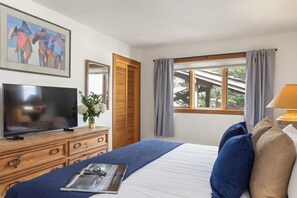 A bedroom with a bed, a TV on a wooden dresser, a window with curtains, and a painting on the wall. - Outpost: Nez Perce D5- Hot Tub Access (Teton Village)