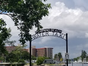 A sign for 'Pompano Beach Water Taxi' with a backdrop of buildings and a cloudy sky. - Beach block cottage with putting green, Everything  needed for a great vacation. (Pompano Beach)