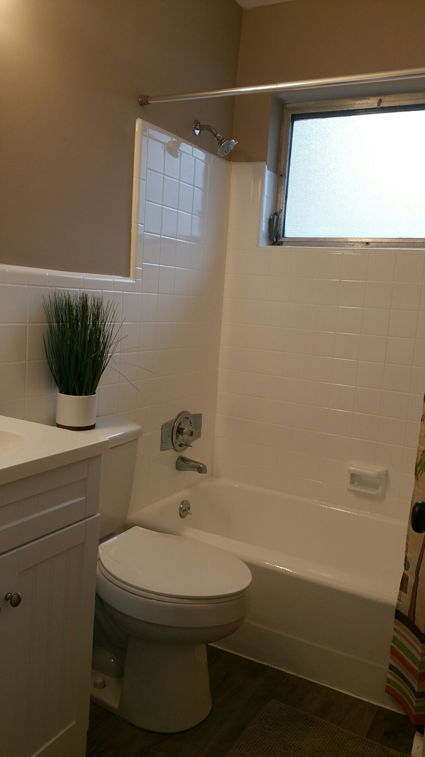 A bathroom with a toilet, bathtub, and a window above the shower.