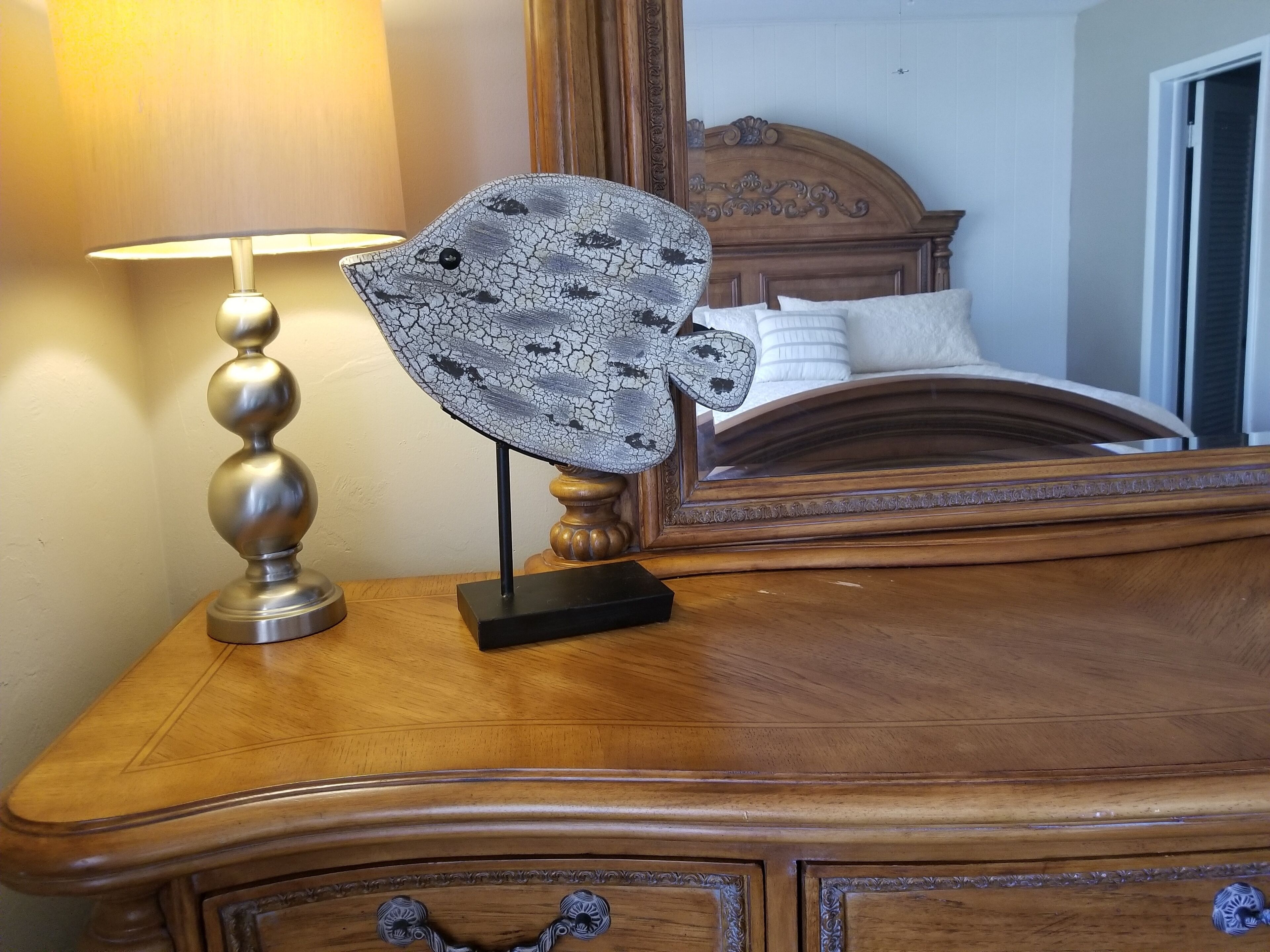 Une commode en bois, sur laquelle sont posés une lampe et une sculpture en forme de poisson.