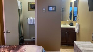 A hotel room with a bed, a bathroom with a sink and mirror, and a door leading to another room. - Winterplace Condo D303 (Ghent)