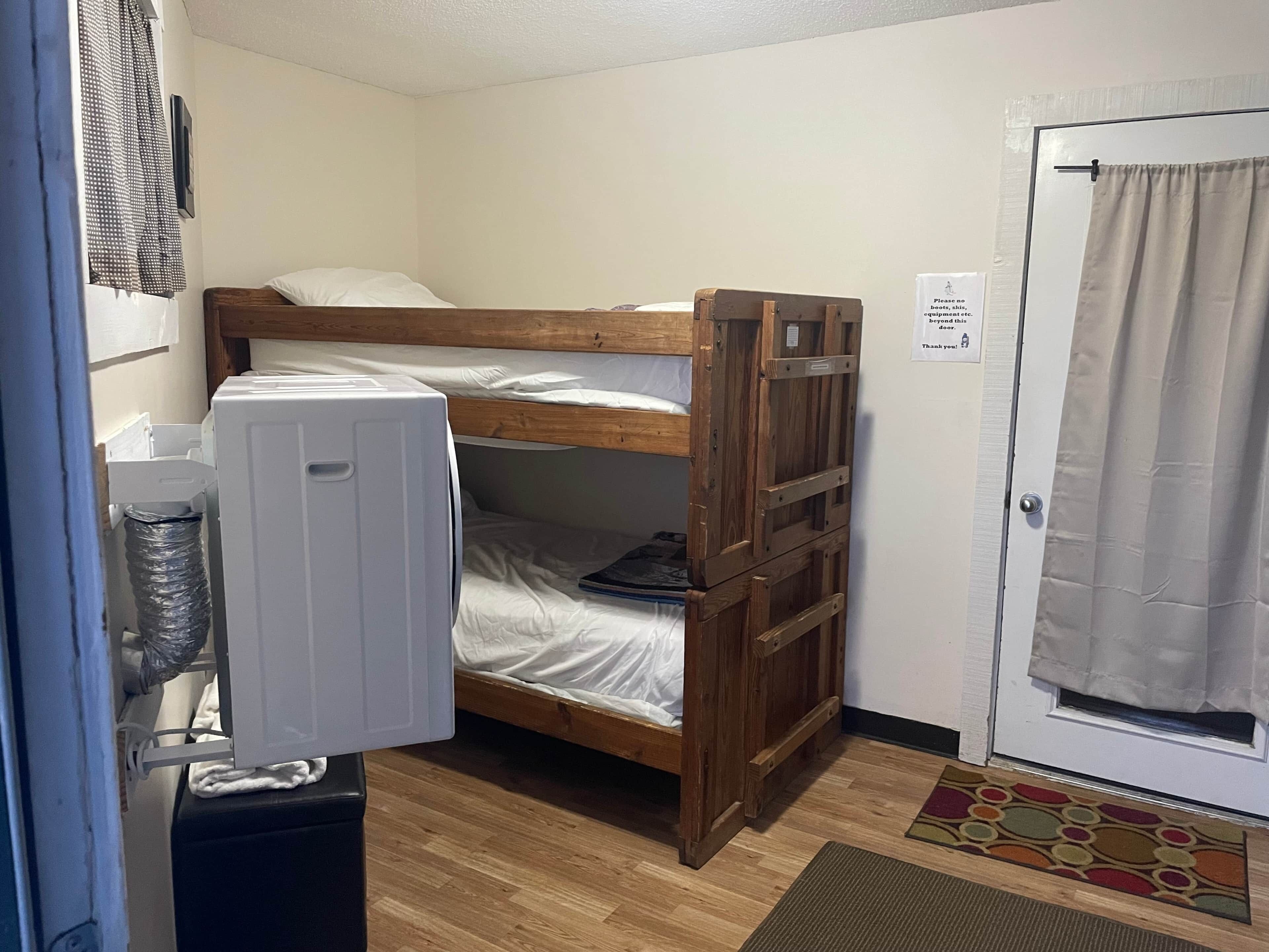 A small room with a bunk bed, a white radiator, a door with a sign, and a patterned rug.