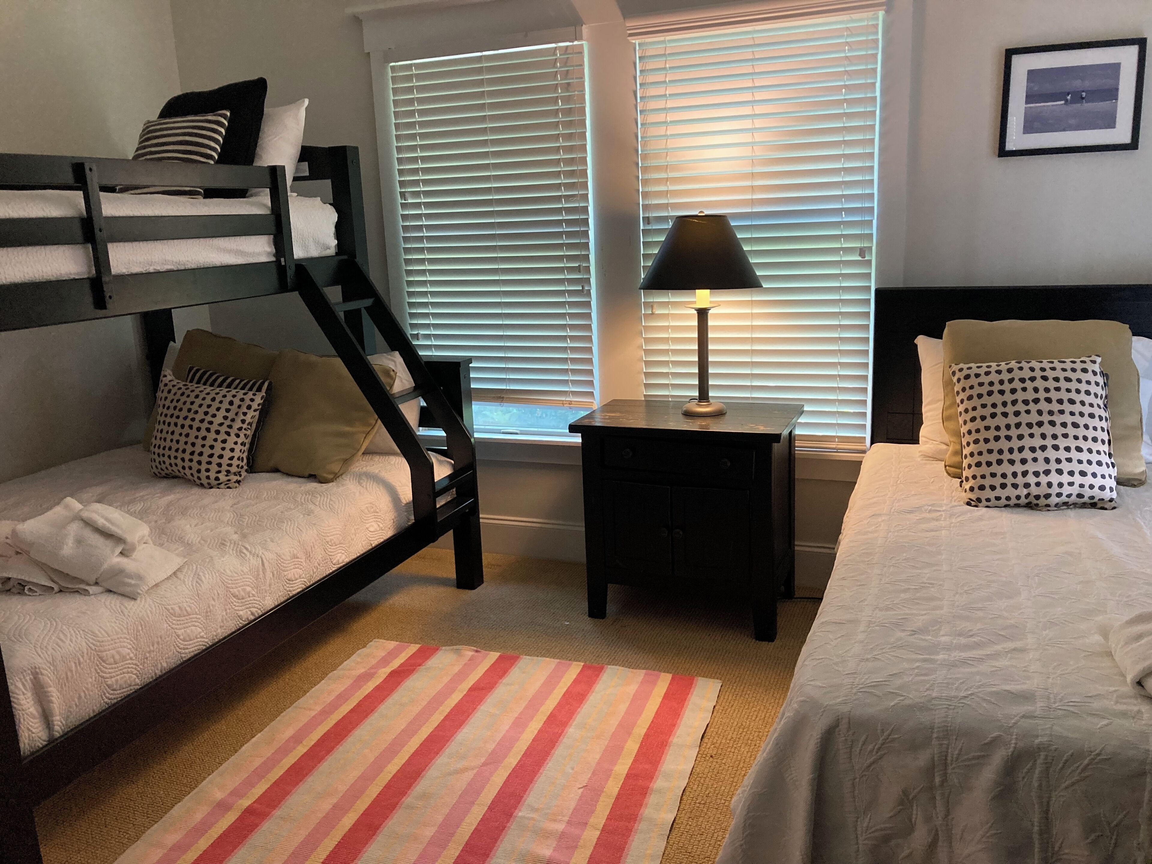A bedroom with bunk beds, a bedside table with a lamp, and a striped rug.