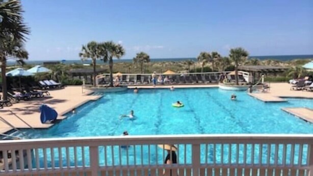 A large outdoor swimming pool with multiple lanes, surrounded by palm trees and a clear sky.
