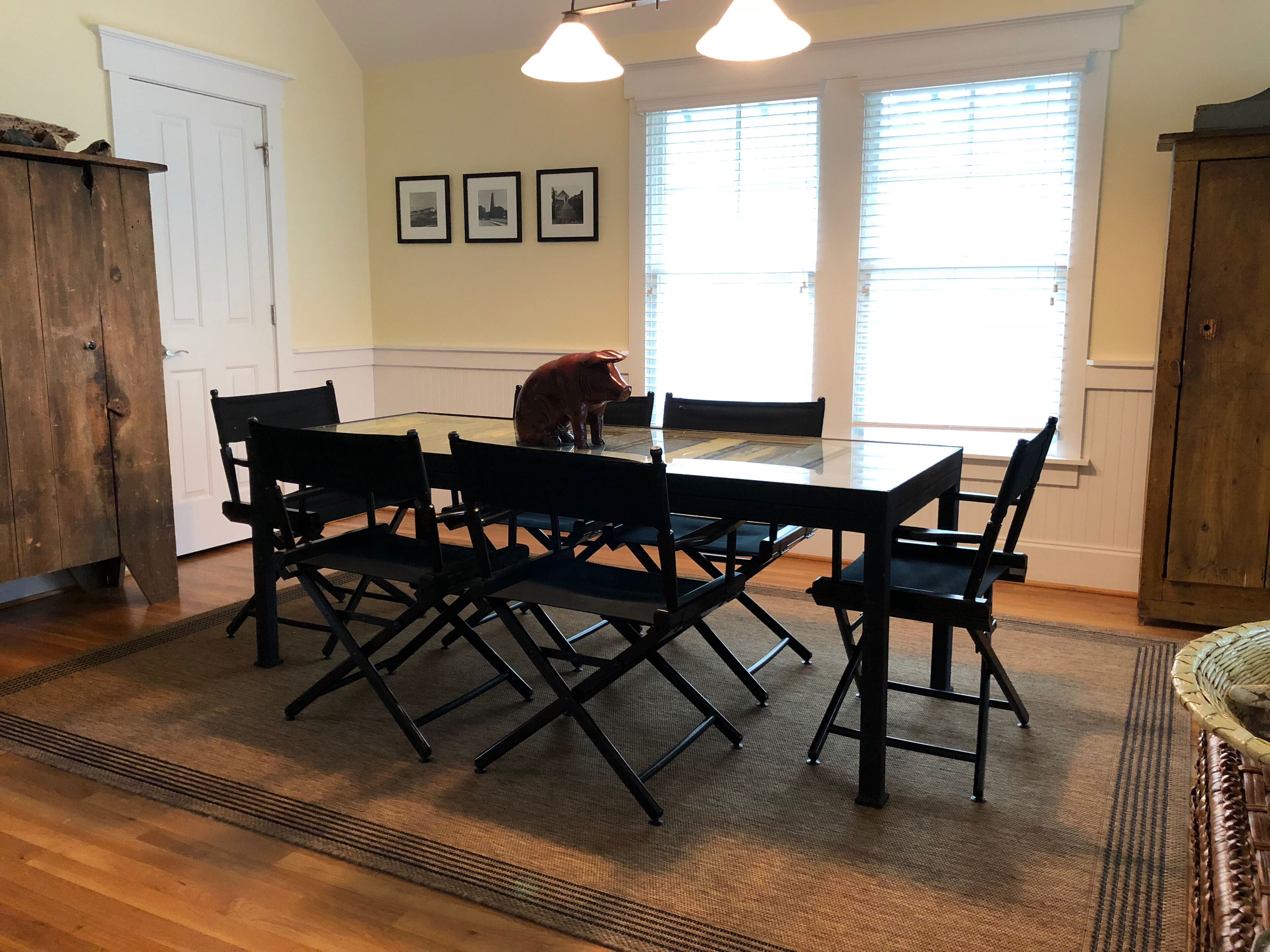A dining room with a glass-top table, black chairs, a wooden cabinet, and a window with blinds.