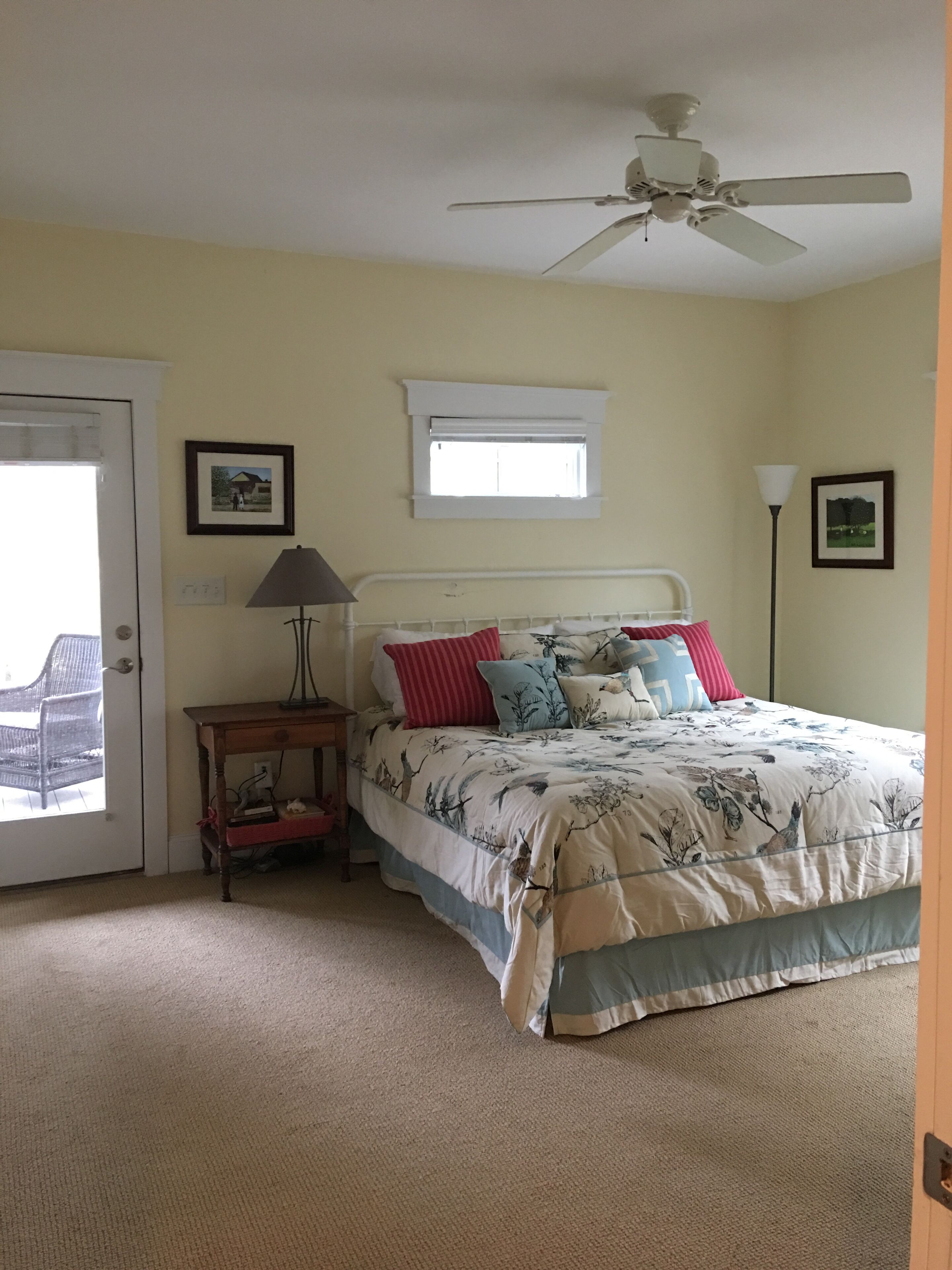 A bedroom with a bed, a nightstand, a ceiling fan, a window, and a door.