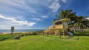 A lifeguard tower with a grassy area, palm trees, and a beach in the background. - Steps to beach! Beautiful renovated 1 bedroom (Kihei)