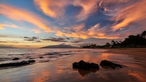 Ein Strand mit ruhigem Wasser, einem Sonnenuntergang und wolkenlosem Himmel.