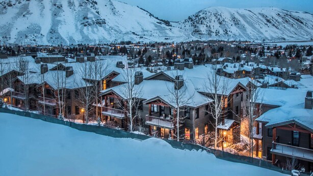 Een besneeuwde plaats met houten huizen en een berg op de achtergrond.