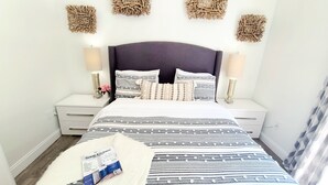 A neatly arranged bedroom with a bed, two bedside tables, and decorative wall hangings. - POSHPADZ - Sandpiper Villa - Walk to Jupiter Beach (Jupiter)