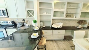 A modern kitchen with a black countertop, white cabinetry, and a built-in stove. There is a small island with a bowl of lemons and a plant. - POSHPADZ - Sandpiper Villa - Walk to Jupiter Beach (Jupiter)