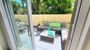 A patio with a glass door, a wicker sofa with cushions, a glass coffee table, and a wooden fence. - POSHPADZ - Sandpiper Villa - Walk to Jupiter Beach (Jupiter)