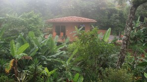 Un petit bâtiment d’un seul étage, doté d’un toit en tuiles et entouré d’une végétation tropicale luxuriante.