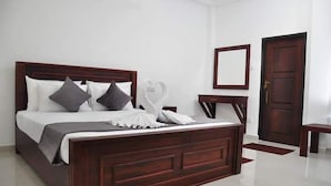 A neatly made bed with a wooden headboard, a bedside table, and a mirror on the wall. - Airport Grand Holiday Home (Seeduwa - Katunayake)