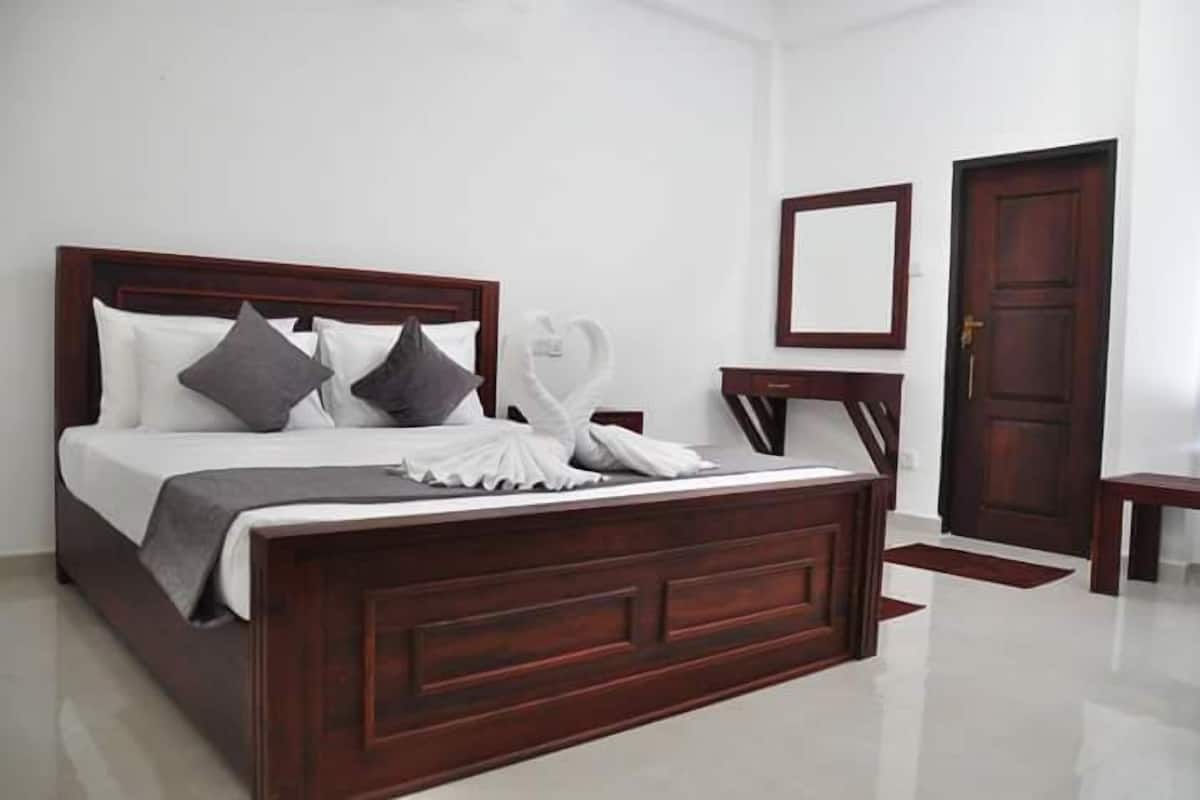 A neatly made bed with a wooden headboard, a bedside table, and a mirror on the wall.