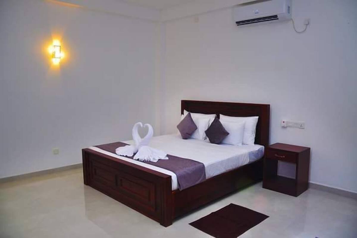 A neatly made bed with a wooden headboard, a bedside table, and a wall-mounted air conditioner.