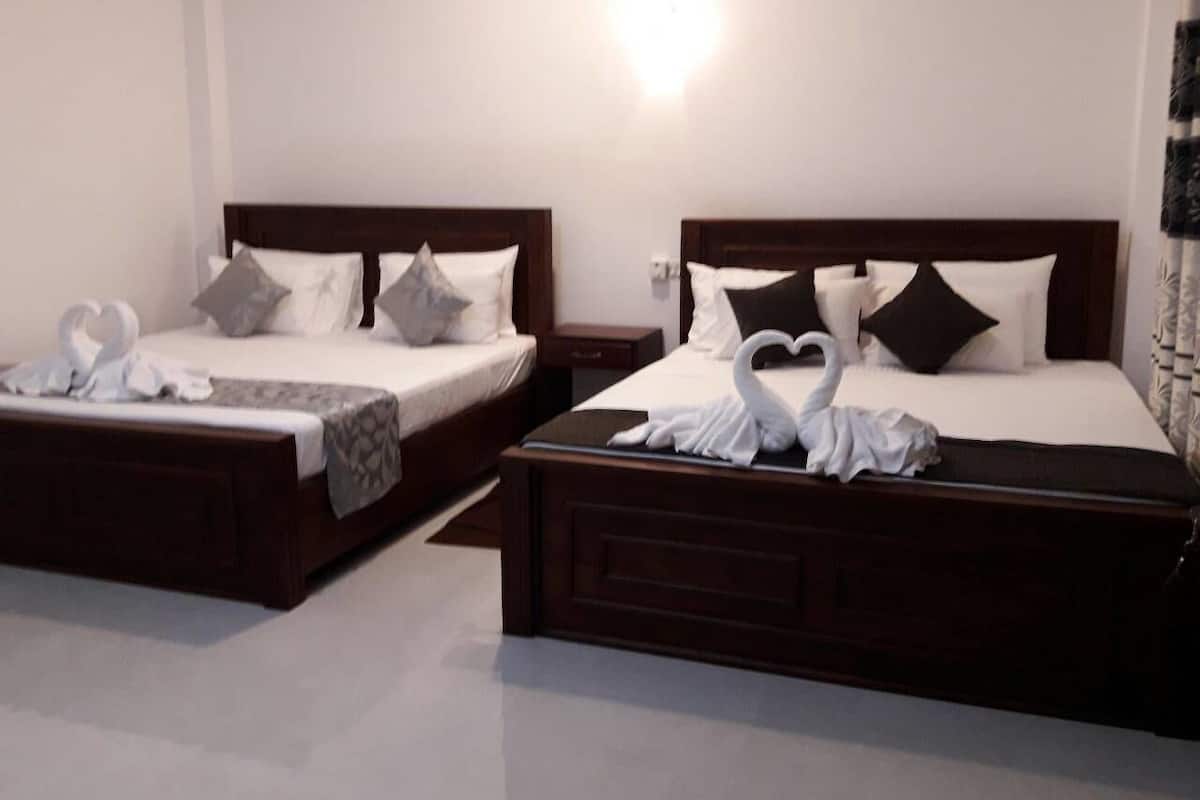 Two twin beds with wooden headboards, white linens, and decorative pillows. Each bed has a small bedside table and a wall-mounted light.