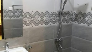 A bathroom with a sink, mirror, shower, and decorative wall tiles. - Airport Grand Holiday Home (Seeduwa - Katunayake)