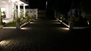 A nighttime view of a building with a gravel driveway, potted plants, and a well-lit entrance. - Airport Grand Holiday Home (Seeduwa - Katunayake)
