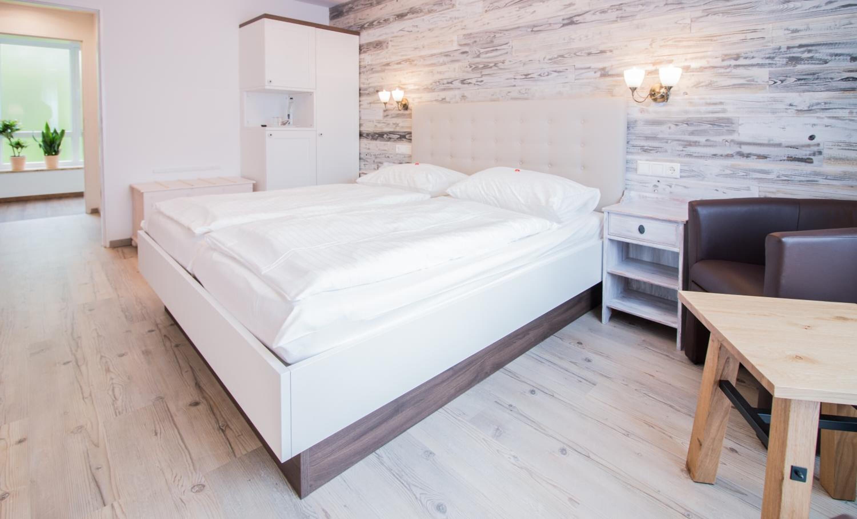 A modern bedroom with a large bed, bedside tables, a wooden nightstand, a desk, and a chair.