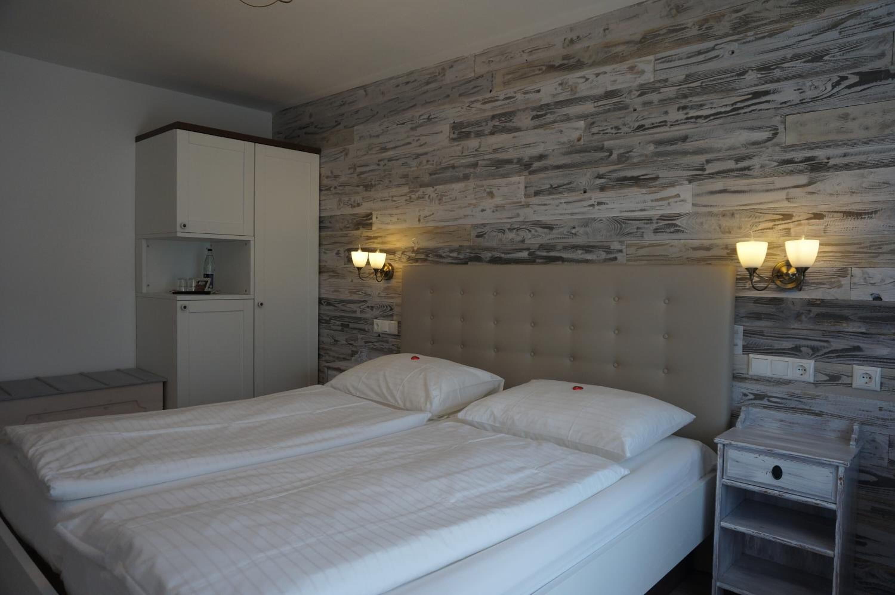Un lit double avec du linge de lit blanc, une armoire et deux appliques murales.